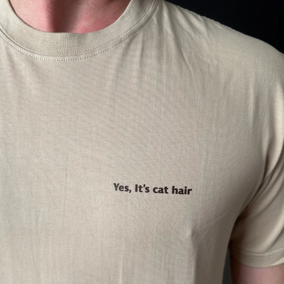 Beige t-shirt with 'Yes, it's cat hair' text on a plain background