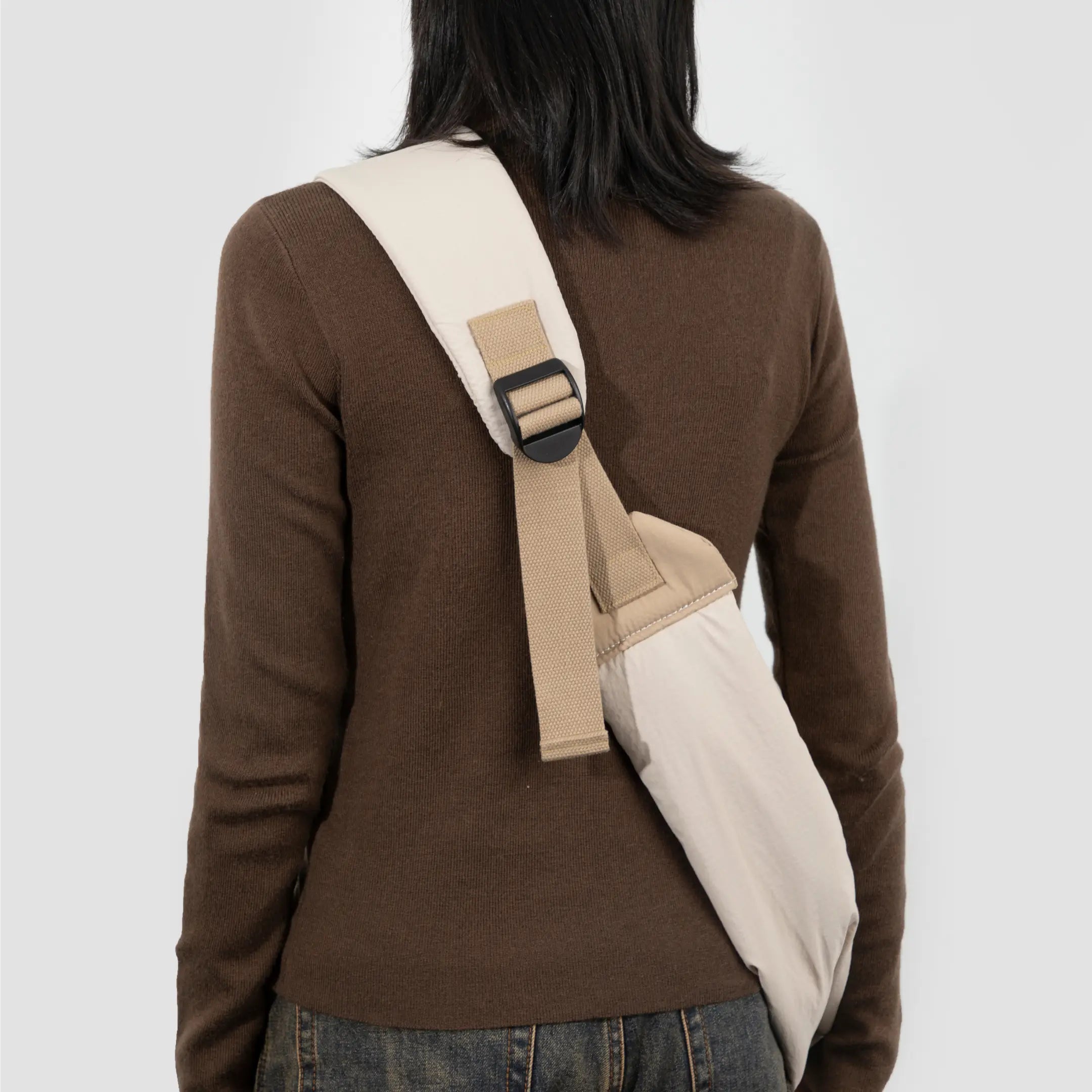 Person wearing a beige tote bag over one shoulder on a white background